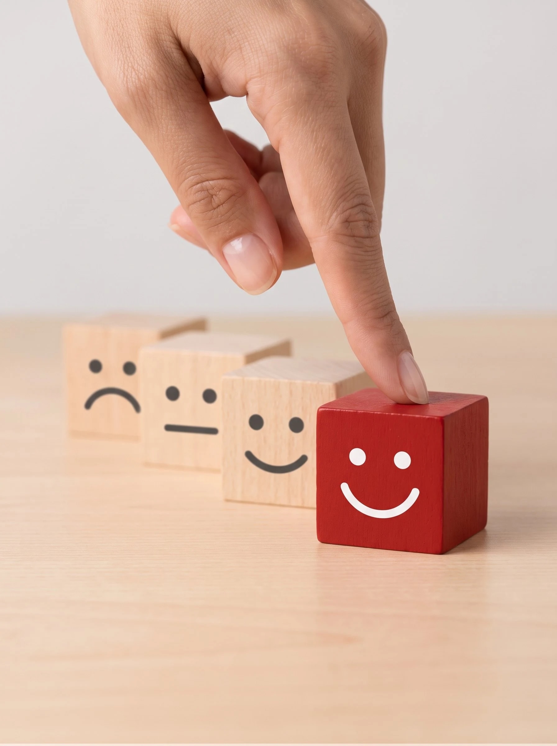 A hand pointing at a red smiling cube beside wooden cubes with other expressions