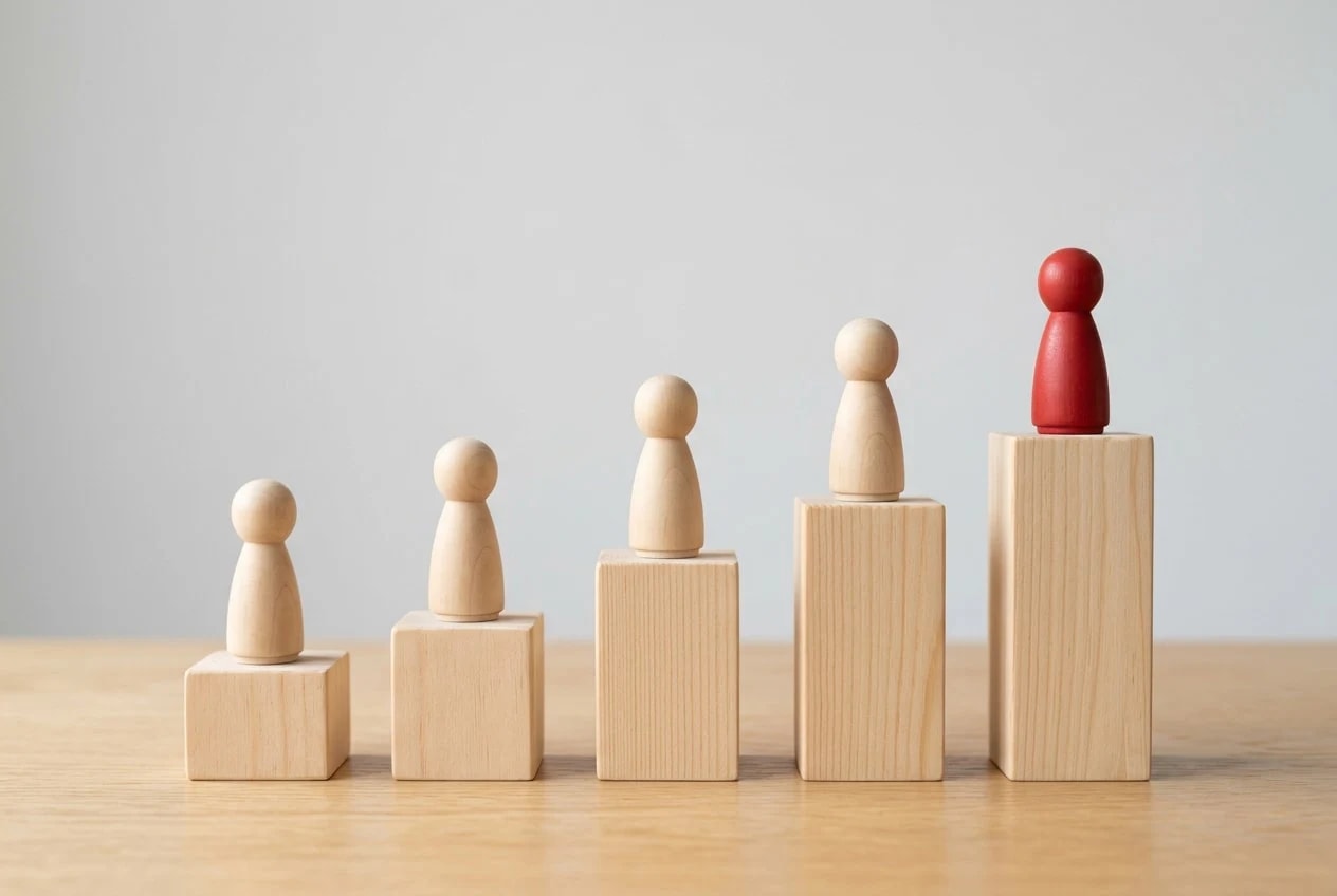 Wooden figures standing on rising wooden blocks, a red figure on the highest block