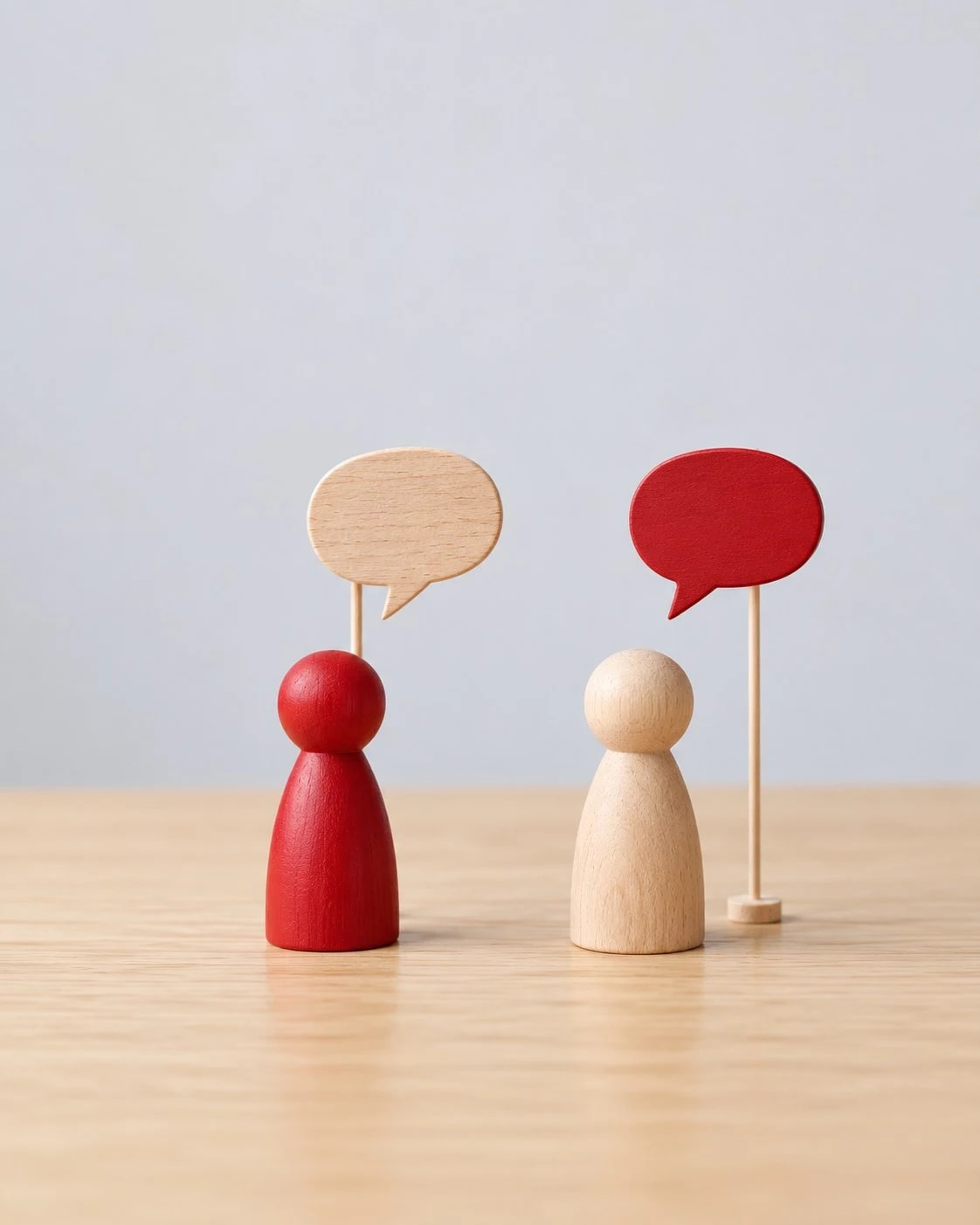 A red and a wooden figure facing each other under wooden speech bubbles